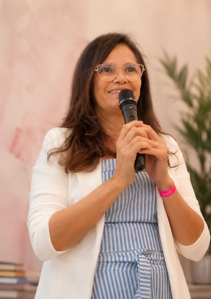 “Alda Leite, criadora do blog Deelas 50+, sorrindo durante uma apresentação, transmitindo acolhimento, experiência e inspiração para mulheres maduras.”