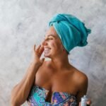 Mulher madura sorridente aplicando protetor solar no rosto em um ambiente iluminado, destacando o cuidado com a pele após os 50 anos