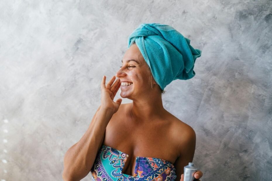 Mulher madura sorridente aplicando protetor solar no rosto em um ambiente iluminado, destacando o cuidado com a pele após os 50 anos