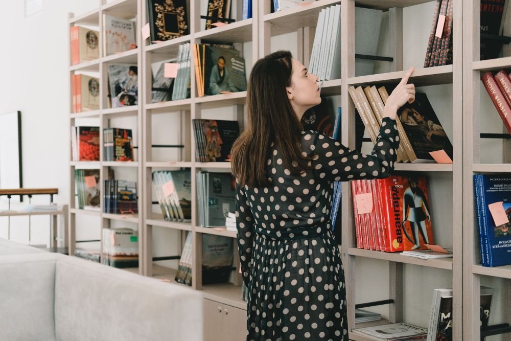 Mulher madura em estante de livros escolhe livros para ler, que tenham temas interessantes, assuntos que fazem sentido para ela.