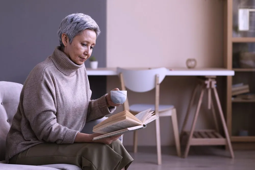 mulher sentada, concentrada em ambiente calmo lendo e tomando café