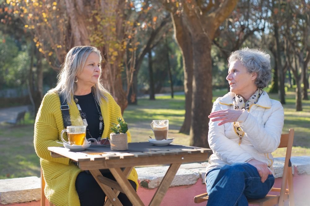 duas mulheres maduras ao ar livre conversando sobre sua leitura enquanto tomam um chá, enquanto conversam fortalecem  a memória